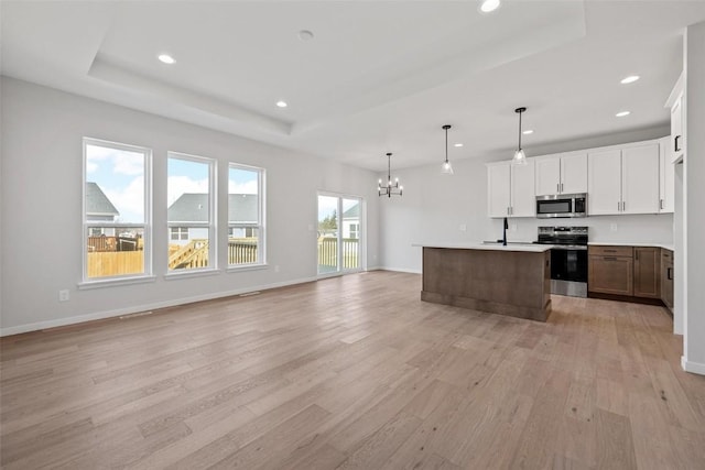 kitchen with a kitchen island with sink, a raised ceiling, appliances with stainless steel finishes, white cabinetry, and decorative light fixtures