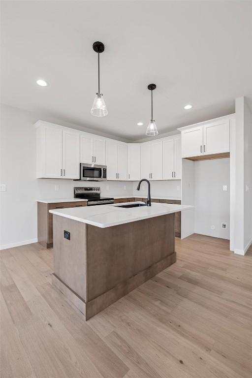 kitchen with sink, stainless steel appliances, an island with sink, and white cabinetry