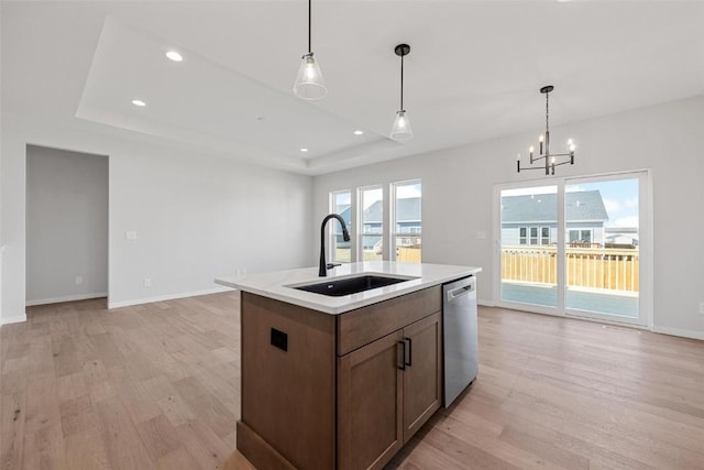 kitchen featuring sink, decorative light fixtures, dishwasher, a tray ceiling, and a kitchen island with sink