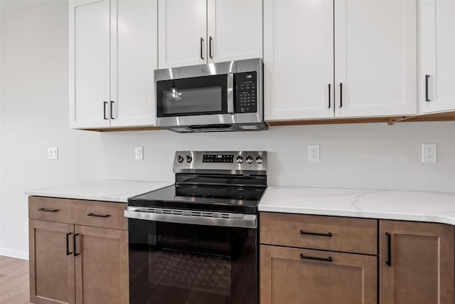 kitchen featuring light stone countertops, appliances with stainless steel finishes, light hardwood / wood-style floors, and white cabinetry