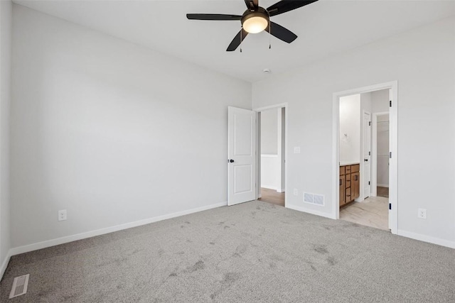 unfurnished bedroom featuring ceiling fan, light colored carpet, and ensuite bath