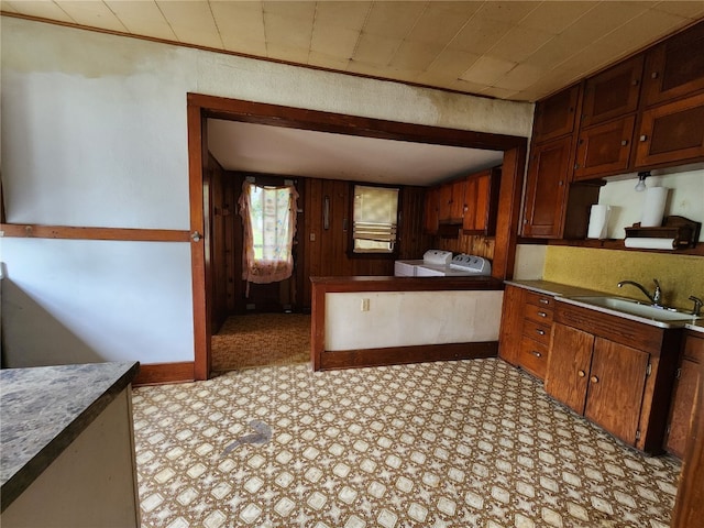 kitchen with sink, wood walls, light tile floors, and washing machine and clothes dryer