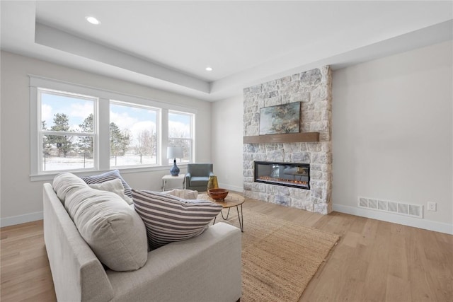 living room featuring light wood-type flooring, a tray ceiling, and a fireplace