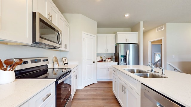 kitchen featuring white cabinets, light wood-type flooring, appliances with stainless steel finishes, light stone counters, and sink