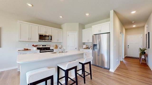 kitchen featuring appliances with stainless steel finishes, light hardwood / wood-style floors, white cabinetry, sink, and a center island with sink