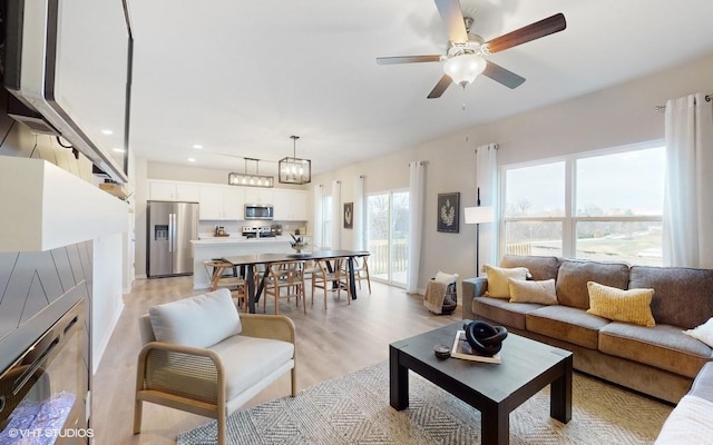 living room featuring ceiling fan with notable chandelier and light wood-type flooring