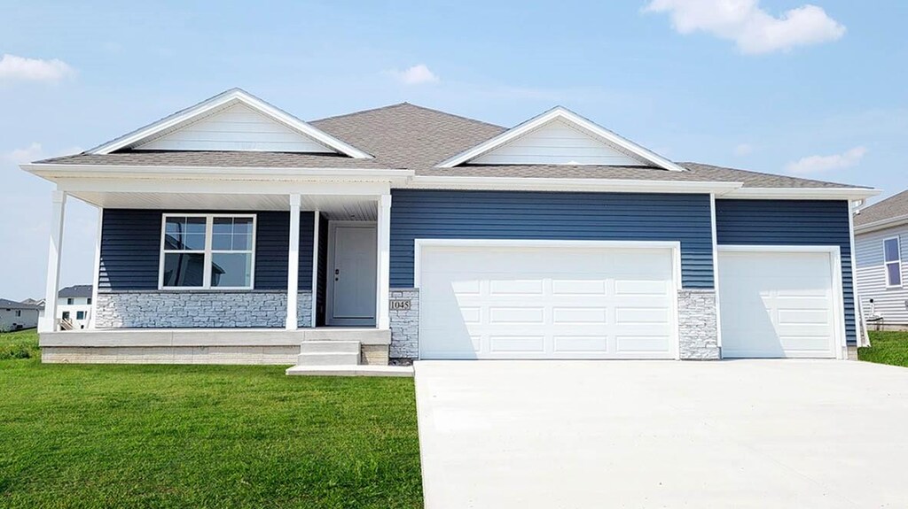 view of front of home with stone siding, an attached garage, a front yard, and driveway