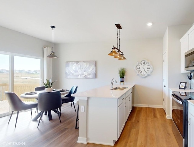 kitchen with white cabinets, light hardwood / wood-style flooring, decorative light fixtures, kitchen peninsula, and stainless steel appliances