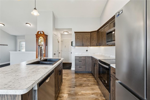 kitchen featuring appliances with stainless steel finishes, dark hardwood / wood-style flooring, sink, hanging light fixtures, and an island with sink