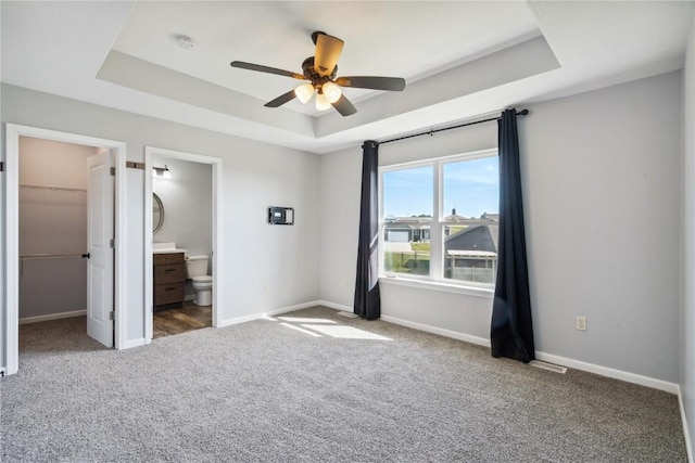 unfurnished bedroom featuring ensuite bath, ceiling fan, a spacious closet, a tray ceiling, and a closet