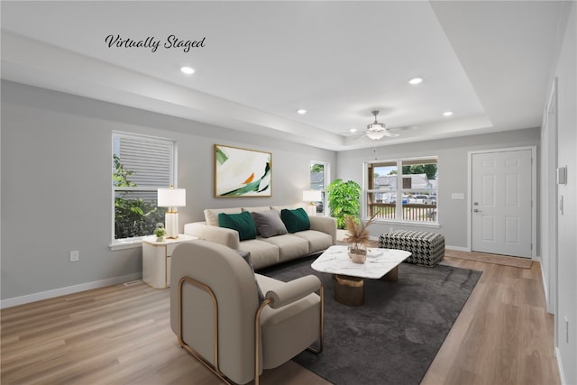 living room with a tray ceiling, light hardwood / wood-style flooring, and ceiling fan