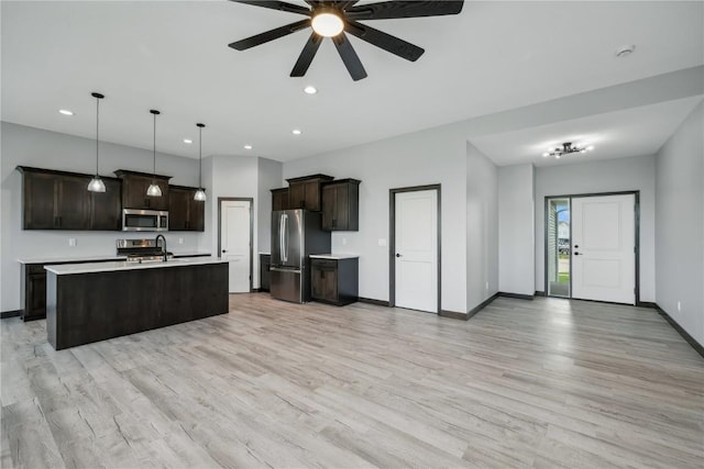 kitchen with pendant lighting, stainless steel appliances, light hardwood / wood-style flooring, and an island with sink