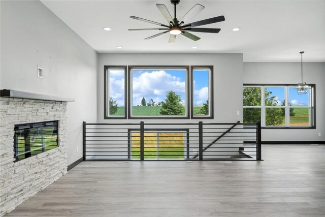 unfurnished living room featuring plenty of natural light, light hardwood / wood-style floors, a stone fireplace, and ceiling fan with notable chandelier