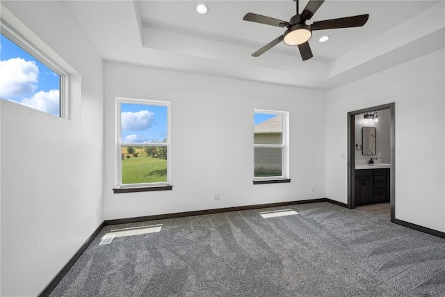 unfurnished bedroom featuring a tray ceiling, multiple windows, ceiling fan, and ensuite bathroom