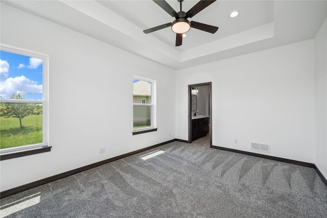 carpeted empty room featuring plenty of natural light, ceiling fan, and a tray ceiling