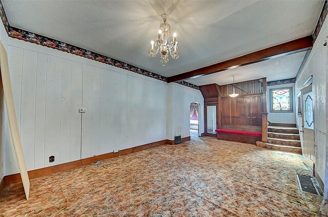 interior space featuring wooden walls, beam ceiling, carpet, a notable chandelier, and a textured ceiling