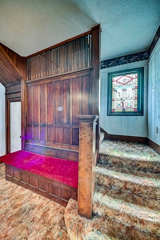 stairs featuring a textured ceiling and wood walls