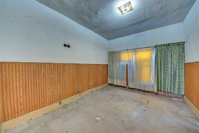 unfurnished room with vaulted ceiling, a textured ceiling, and wood walls