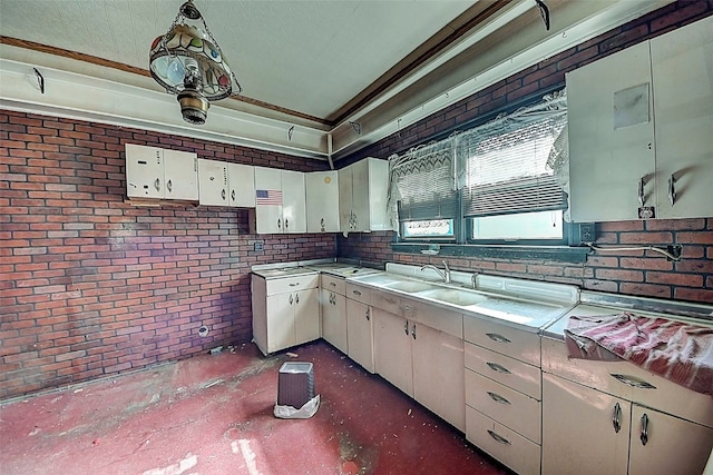 kitchen featuring brick wall, white cabinetry, sink, hanging light fixtures, and ornamental molding