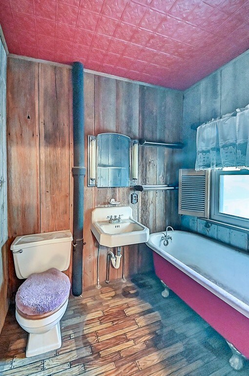 bathroom featuring sink, wood-type flooring, a tub to relax in, toilet, and wood walls