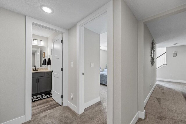 hall with sink, light colored carpet, and a textured ceiling