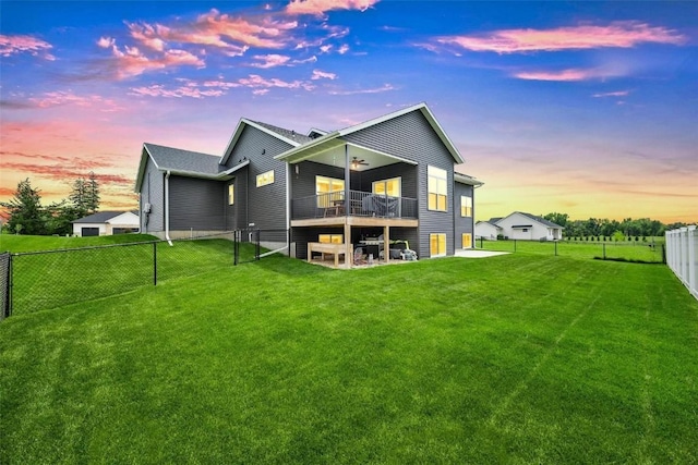 back house at dusk with a yard, ceiling fan, and a balcony