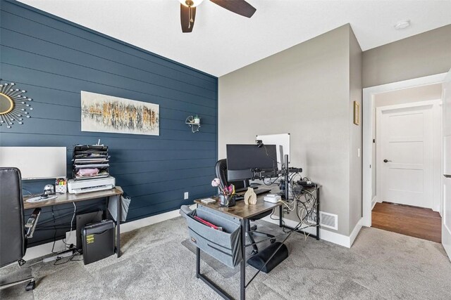 office space featuring carpet, ceiling fan, and wood walls