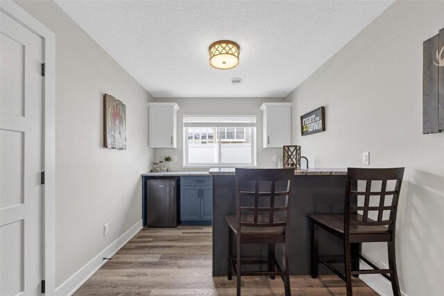 bar with white cabinetry, light hardwood / wood-style flooring, refrigerator, and a textured ceiling