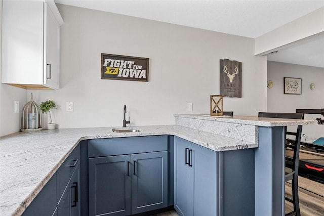 kitchen with white cabinetry, sink, a kitchen breakfast bar, light stone counters, and kitchen peninsula