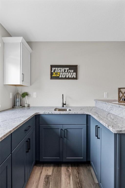 kitchen featuring white cabinets, blue cabinets, sink, hardwood / wood-style flooring, and light stone countertops