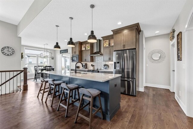 kitchen with stainless steel fridge, backsplash, dark wood-type flooring, decorative light fixtures, and an island with sink