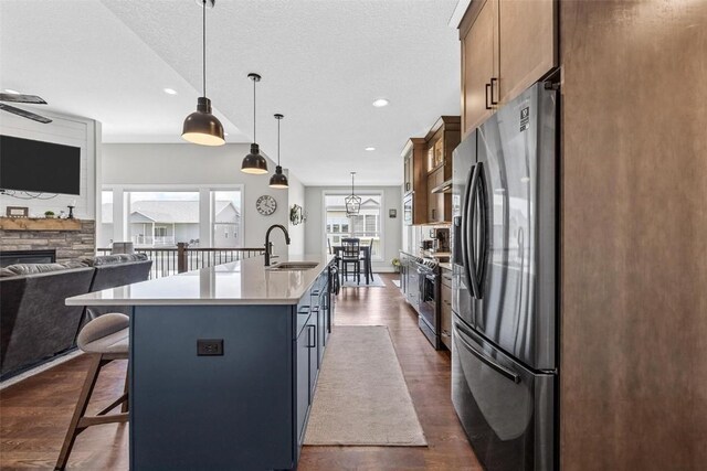 kitchen featuring sink, stainless steel appliances, dark hardwood / wood-style flooring, decorative light fixtures, and a center island with sink