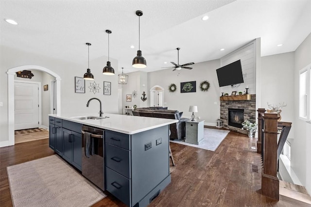 kitchen featuring an island with sink, light countertops, dishwashing machine, arched walkways, and a sink