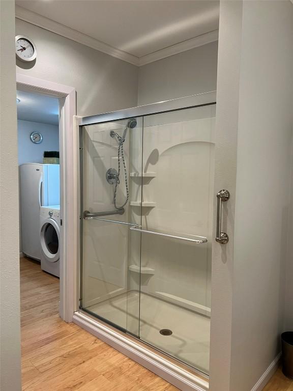 bathroom featuring washer / dryer, crown molding, wood finished floors, and a stall shower