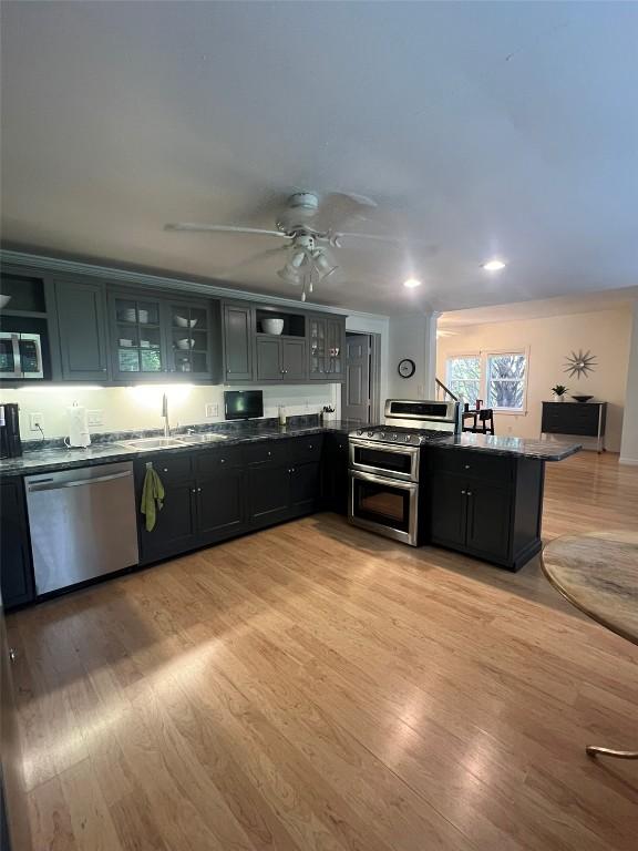 kitchen featuring ceiling fan, a sink, appliances with stainless steel finishes, light wood finished floors, and glass insert cabinets