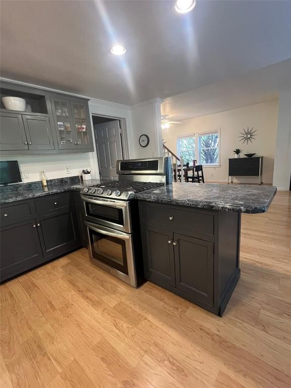 kitchen with a peninsula, double oven range, dark stone counters, light wood finished floors, and glass insert cabinets