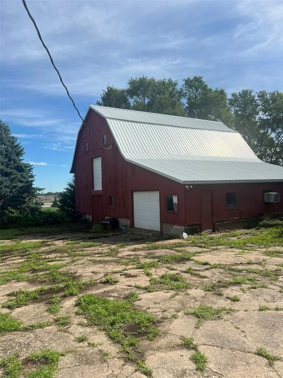 view of home's exterior with a gambrel roof, metal roof, a barn, a garage, and driveway