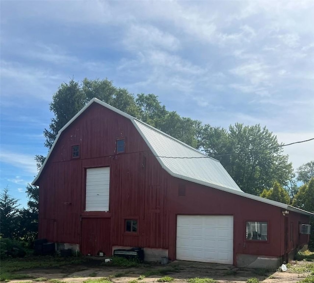 view of side of home featuring a barn, a gambrel roof, a detached garage, metal roof, and an outbuilding