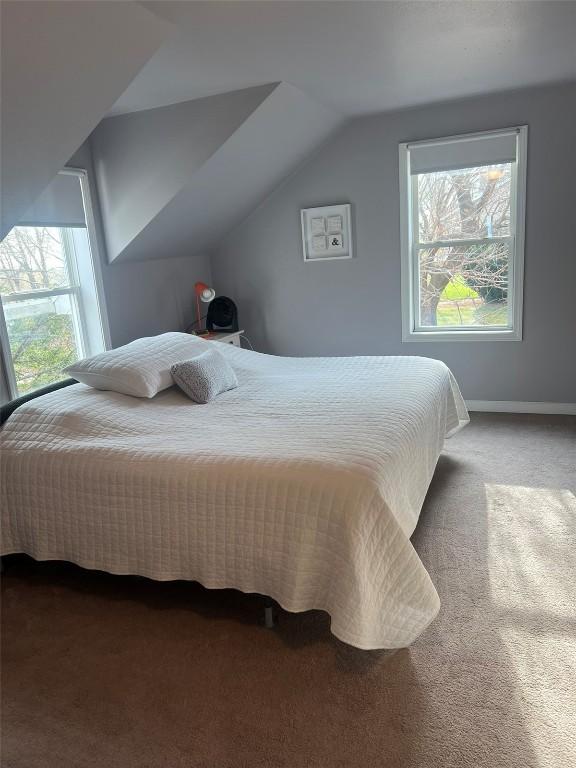 carpeted bedroom with multiple windows, vaulted ceiling, and baseboards