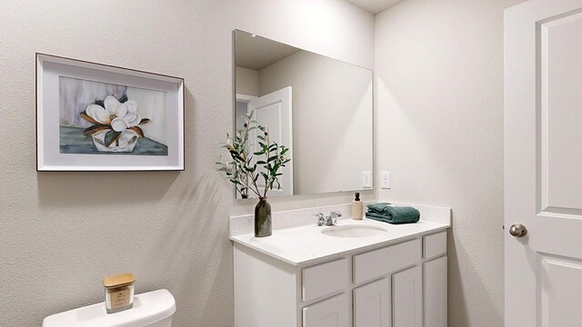 half bath with vanity, toilet, and a textured wall