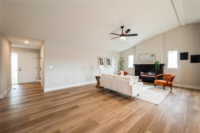 living room with ceiling fan, high vaulted ceiling, baseboards, light wood finished floors, and a glass covered fireplace