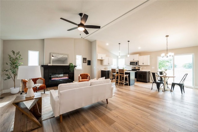 living room with lofted ceiling, light hardwood / wood-style flooring, and ceiling fan with notable chandelier