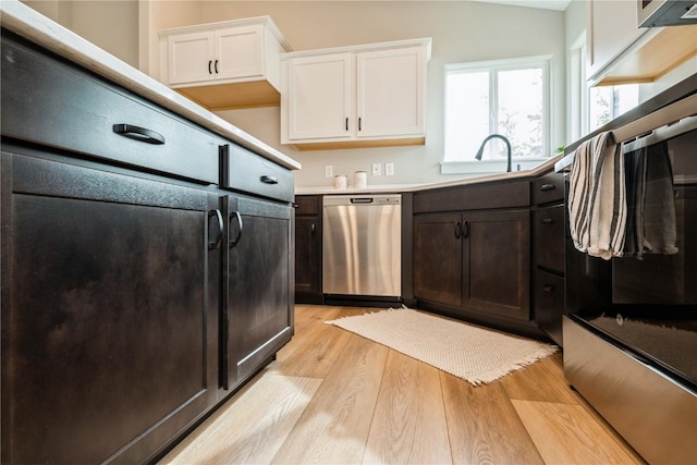 kitchen featuring light countertops, stainless steel dishwasher, light wood-style floors, white cabinetry, and a sink