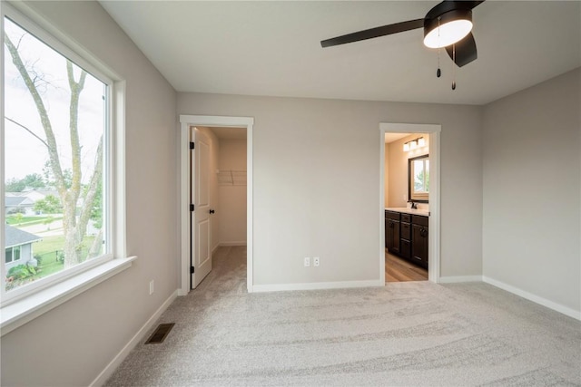 unfurnished bedroom featuring light carpet, baseboards, visible vents, ensuite bath, and a walk in closet