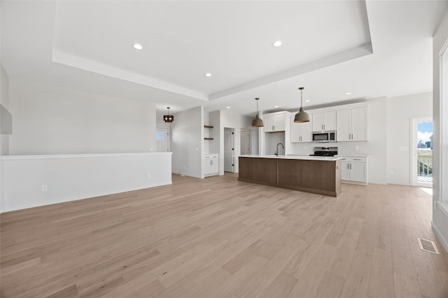 kitchen featuring a raised ceiling, white cabinetry, appliances with stainless steel finishes, and a kitchen island with sink