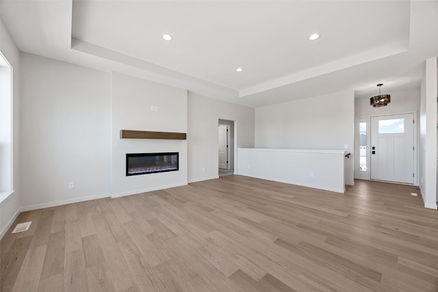 unfurnished living room with a chandelier, a raised ceiling, and light hardwood / wood-style flooring