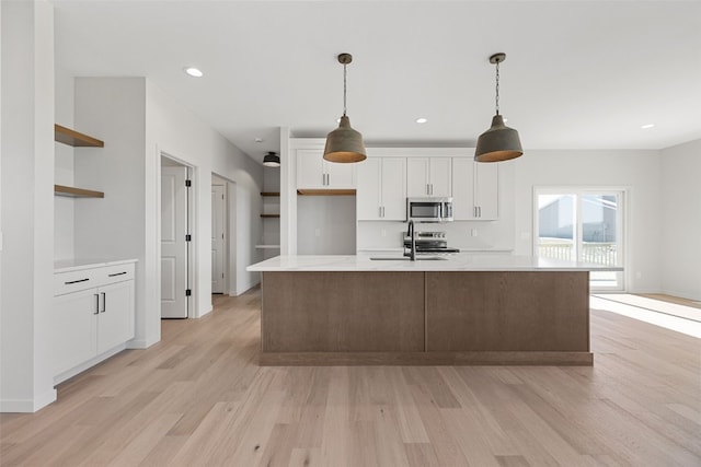 kitchen featuring appliances with stainless steel finishes, white cabinets, hanging light fixtures, a kitchen island with sink, and light hardwood / wood-style floors