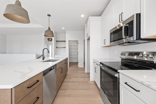 kitchen featuring pendant lighting, sink, white cabinetry, stainless steel appliances, and light stone countertops