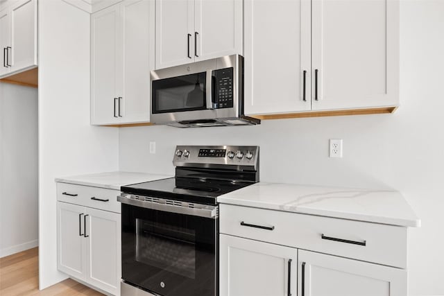 kitchen with white cabinetry, stainless steel appliances, light stone counters, and light hardwood / wood-style flooring