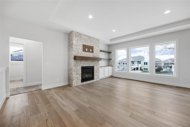 unfurnished living room with a tray ceiling, a fireplace, a healthy amount of sunlight, and light wood-type flooring